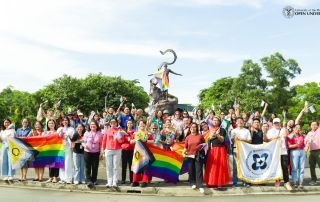 The UPOU staff, faculty, students, and partners hold up colorful Pride Flags in front of the UPOU Oblation as part of the Wear Your Pride 2025.